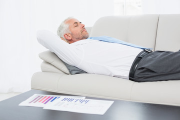 Fototapeta premium Businessman sleeping on sofa with graphs on table in living room