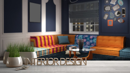 Wooden table, desk or shelf with potted grass plant, house keys and 3D letters making the words interior design, over blurred colored living room