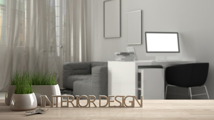 Wooden table, desk or shelf with potted grass plant, house keys and 3D letters making the words interior design, over blurred modern workplace, project concept copy space background