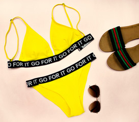 Naklejka premium Summer set of clothes on a pink background consisting of yellow swimsuit, yellow hat, glasses and flip-flops