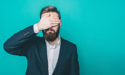 Silent man is standing and covering his eyes witha hand. Isolated on blue background.