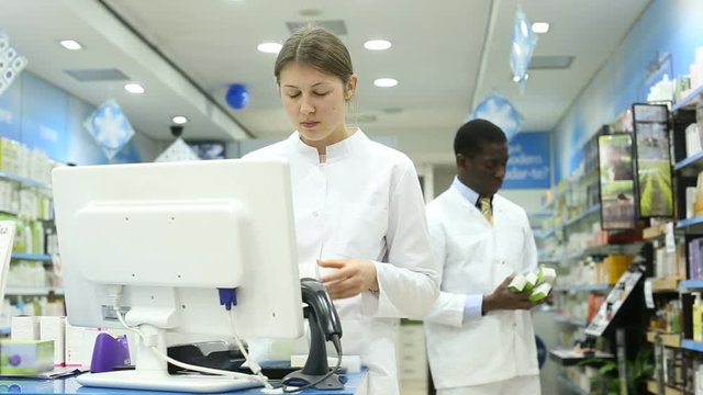 Experienced female pharmacist standing on background with male colleague in pharmacy