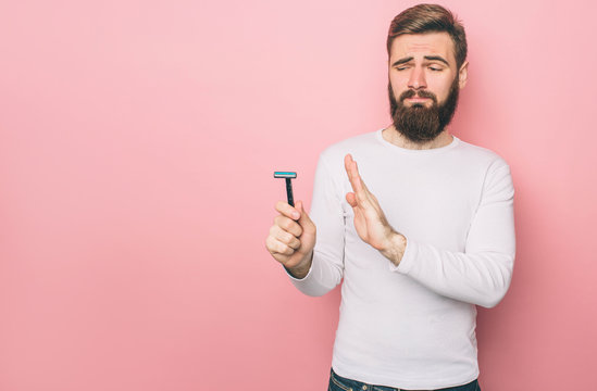 Man is holding a razer in his hand. He is looking at it with disgust. Isolated on pink background.