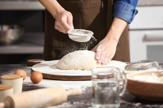 Woman sprinkling flour over dough on table in kitchen