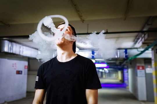 Man in cap smoke an electronic cigarette and releases clouds of vapor performing various kind of vaping tricks