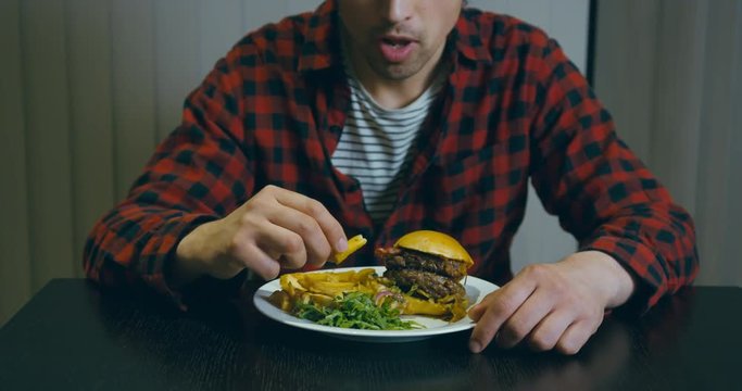 Young man eating hamburger at table