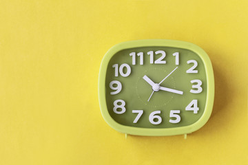Green clock with white numbers and arrows on yellow background