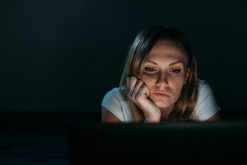 Beautiful girl is bored in front of a laptop at night. Isolated black. Front view. insomnia.