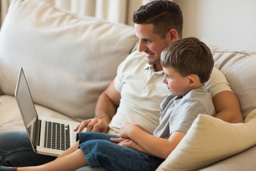 Relaxed father and son using laptop on sofa