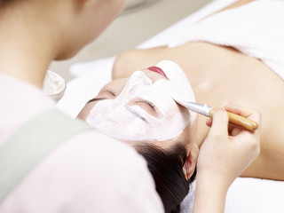 Obraz na płótnie Canvas asian beautician applying facial mask on face of young woman