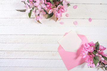 Сard with an pink envelope and pink flowers of apple tree on wooden board.