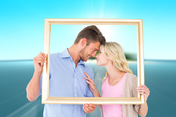 Attractive young couple holding picture frame against tropical island in blue ocean