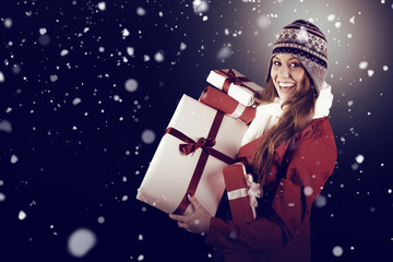 Pretty redhead in warm clothing holding gifts against snow