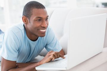 Relaxed casual Afro man with laptop lying on sofa