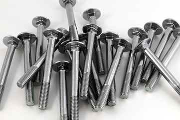 Heap of metal bolts of chrome steel with a round head and incomplete thread on a white background.