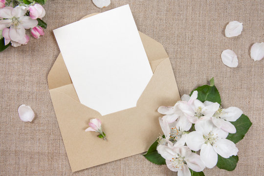 Сard with an beige envelope and white flowers of apple tree on beige fabric.