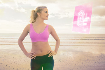 Toned woman with hands on hips on beach against fitness interface