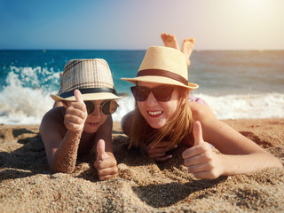 Mom and son in sunglasses are having fun on the beach against the sea. They are holding thumbs up. - 202675979