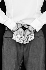 Businessman in handcuffs holding bribe against black background
