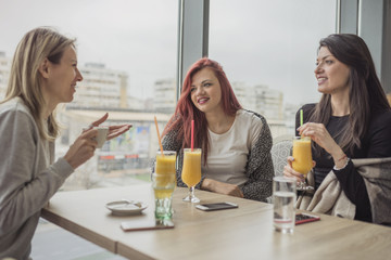 Portrait of three young beautiful women using mobile phone at coffee shop.