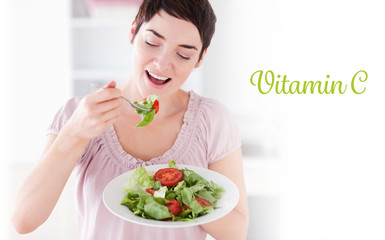 The word vitamin c against smiling woman eating salad