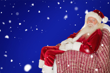 Smiling santa relaxing on the armchair against red background