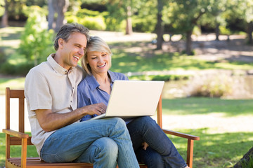 Couple using laptop on park bench