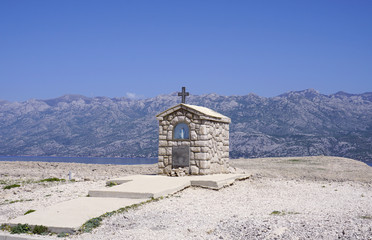 Fototapeta premium Small stone chapel with Mary statue in front of mountain Velebit in Croatia