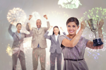Woman holding up a cup with enthusiastic coworkers against colourful fireworks exploding on black background
