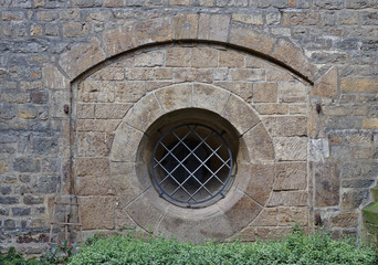 Ancient sandstone wall with arch and barred round window