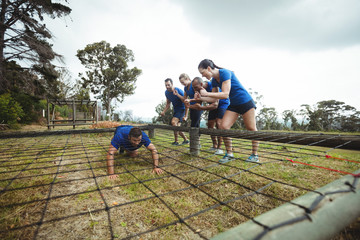 Fit man crawling under the net during obstacle course while fit people cheering
