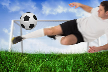 Football player in white kicking ball against field of grass under blue sky