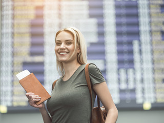 Portrait of cheerful young woman holding password in hands while locating in airport