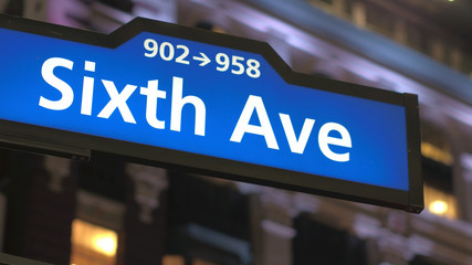 CLOSE UP: Glowing blue Sixth Avenue street sign against stunning office building