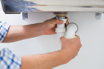 Plumbers hands and washbasin drain at bathroom