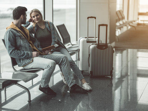 Full length male telling with outgoing girl while they sitting in lounge zone. Positive communication before journey concept