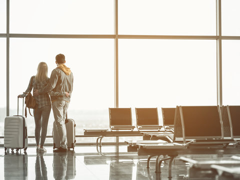 Full Length Man Hugging Lady In Airport. They Looking At Street. Male And Girlfriend In Airport Concept