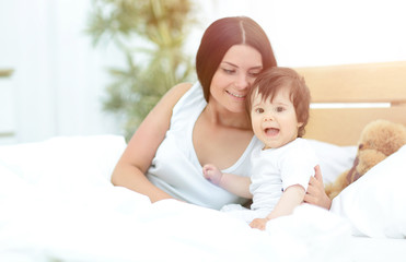 Beautiful young mother  with a baby  lying in bed and smiling