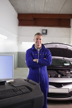Mechanic next to a car and a computer with arms crossed