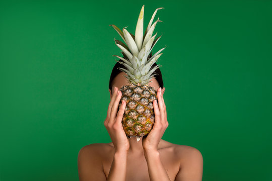 Young girl covering face with pineapple. Her shoulders are naked. Isolated on background