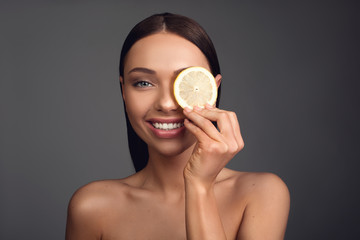 Eco concept. Undressed and happy woman staring at camera while holding fruit cut in front of eye. Isolated on background