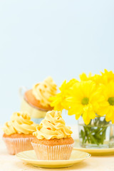 Cupcake with yellow cream decoration and bouquet of yellow chrysanthemum in glass on tender pastel background.