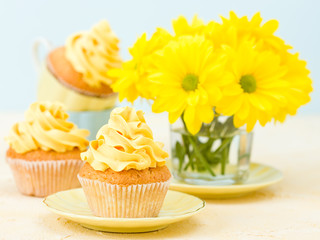 Cupcake with yellow cream decoration and bouquet of yellow chrysanthemum in glass on tender pastel background.