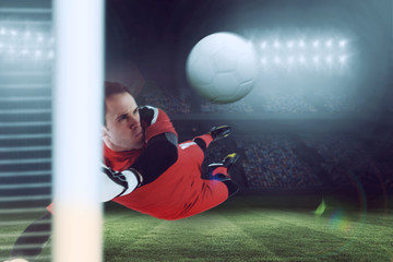 Fit goal keeper jumping up against large football stadium under blue sky