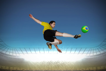 Fototapeta na wymiar Football player in yellow kicking against large football stadium with spotlights under bright blue sky
