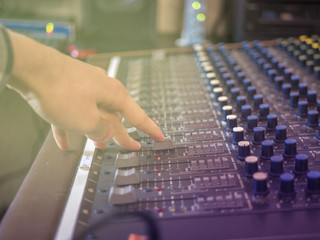close up hand adjusting volume on music recording panel with faders