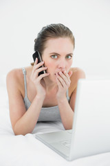 Portrait of a shocked casual woman using cellphone and laptop