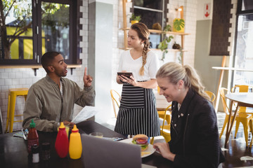 Young man ordering food to waitress while sitting with female friend