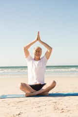 Fototapeta na wymiar Senior man sitting on mat while meditating at beach