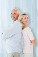 Smiling couple standing leaning backs together against bleached wooden planks background